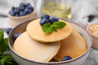 Photo of Bowl with tasty oatmeal pancakes, mint and blueberries on table, closeup