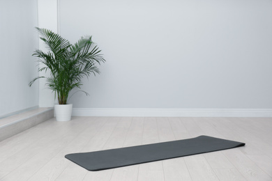 Photo of Unrolled black yoga mat on floor in room. Space for text