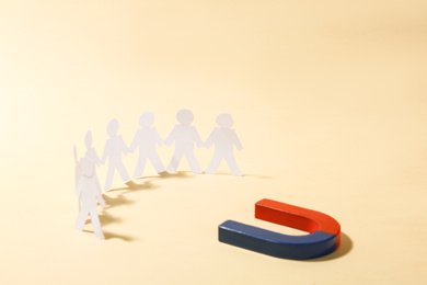 Magnet attracting paper people on beige background