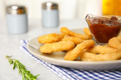 Delicious crunchy fried onion rings and rosemary on light table, closeup