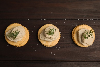 Delicious crackers with humus and dill on wooden table, flat lay