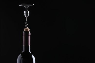Opening wine bottle with corkscrew on dark background, closeup. Space for text