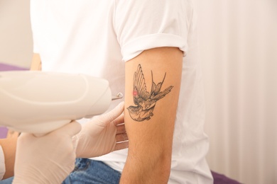 Young man undergoing laser tattoo removal procedure in salon, closeup