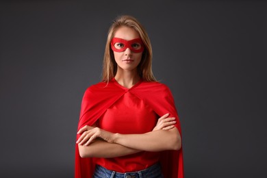 Confident woman wearing superhero cape and mask on grey background