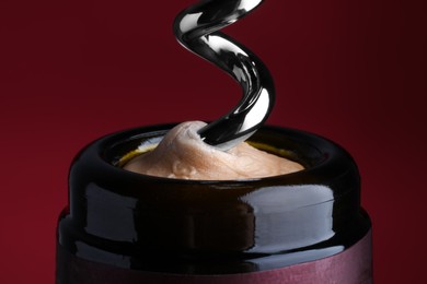 Opening bottle of wine with corkscrew on burgundy background, closeup