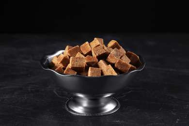 Metal bowl with brown sugar cubes on black table