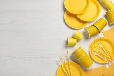 Yellow disposable tableware on white wooden background, flat lay. Space for text