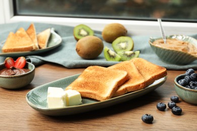 Tasty toasts and different toppings on wooden table at window