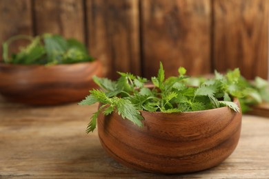 Photo of Fresh stinging nettle leaves in bowl on wooden table