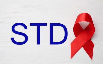 Red awareness ribbon and abbreviation STD on white wooden background, top view 