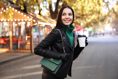 Beautiful young woman with cup of coffee on city street. Autumn walk