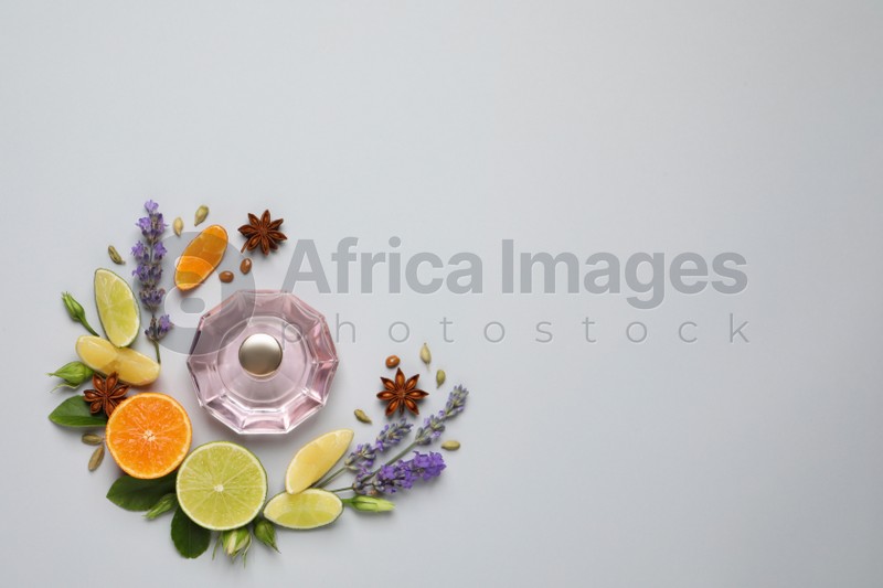 Flat lay composition with bottle of perfume, citrus fruits and flowers on light grey background. Space for text