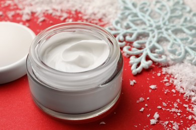 Photo of Winter skin care. Hand cream near decorative snowflake on red background, closeup