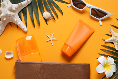 Flat lay composition with sun protection products and beach accessories on orange background