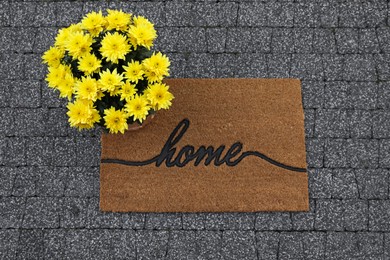 Photo of Doormat with word Home and flowers on pavement, flat lay