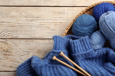 Soft blue woolen yarns, knitting needles and sweater on white wooden background, flat lay. Space for text