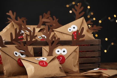 Gifts in envelopes with deer faces on wooden table against blurred lights. Christmas advent calendar