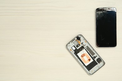 Damaged smartphone on white wooden background, flat lay with space for text. Device repairing