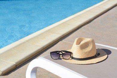 Photo of Stylish straw hat and sunglasses on grey sunbed at poolside. Beach accessories