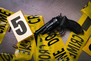 Photo of Flat lay with yellow tape, crime scene marker and gun on grey stone background