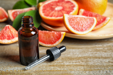 Citrus essential oil and grapefruits on wooden table. Space for text