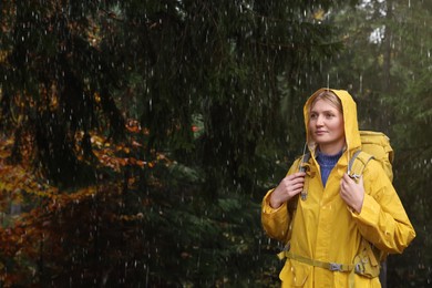 Photo of Young woman with raincoat and backpack in forest under rain