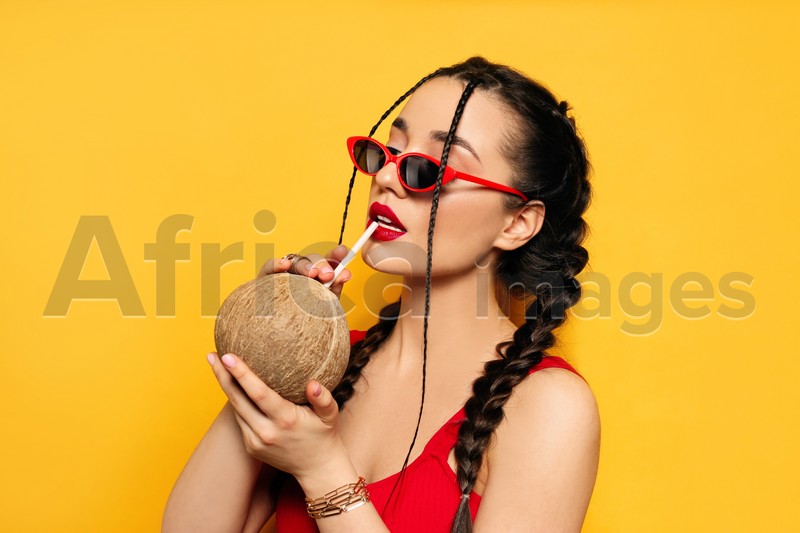 Photo of Young woman with fresh coconut on yellow background. Exotic fruit