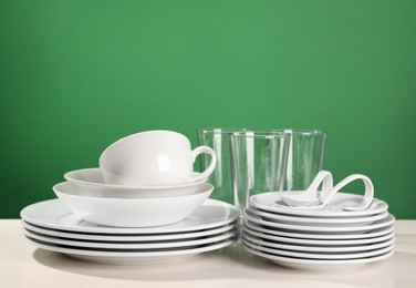 Photo of Set of clean dishware on white table against green background