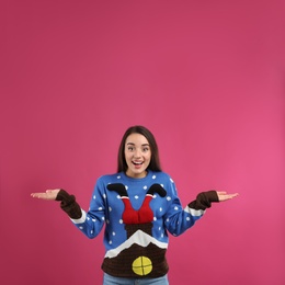 Surprised young woman in Christmas sweater on pink background, space for text