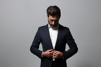 Elegant bearded man adjusting blazer on light grey background