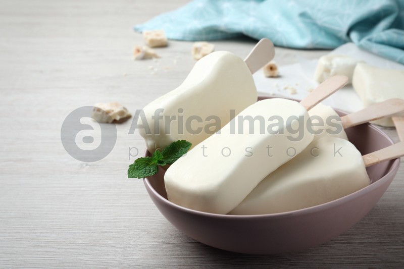 Photo of Delicious glazed ice cream bars, chocolate and mint on white wooden table. Space for text