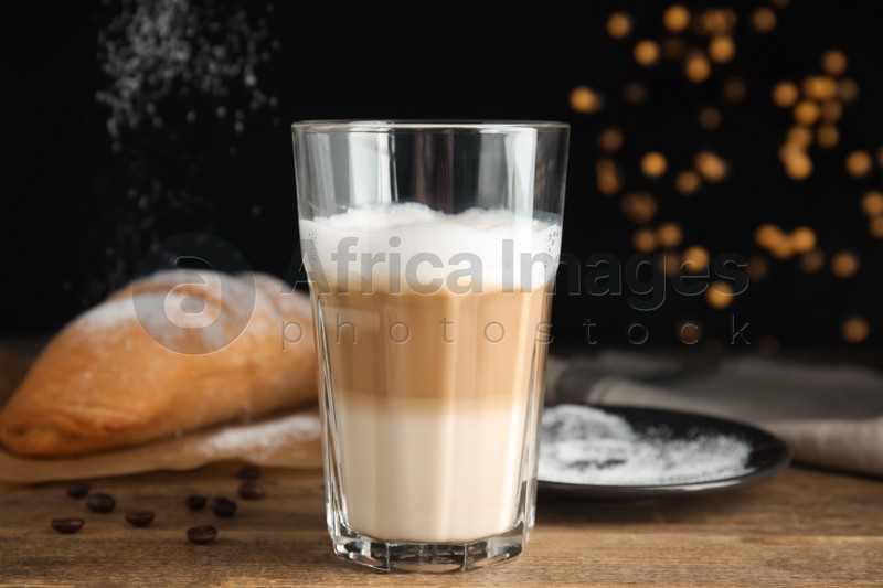 Delicious latte macchiato, croissant and scattered coffee beans on wooden table