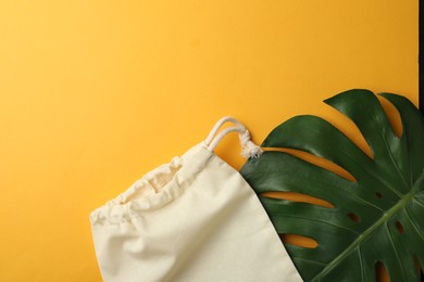 Photo of Cotton eco bag and leaf on yellow background, flat lay. Space for text
