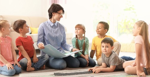 Young woman reading book to little children indoors. Banner design