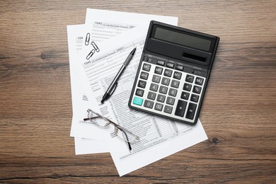 Calculator, glasses, documents and stationery on wooden table, flat lay. Tax accounting