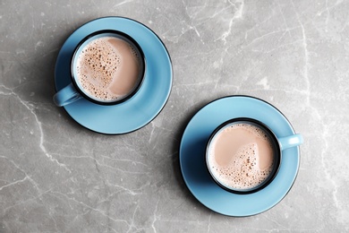 Cups with hot cocoa drink on grey table, top view