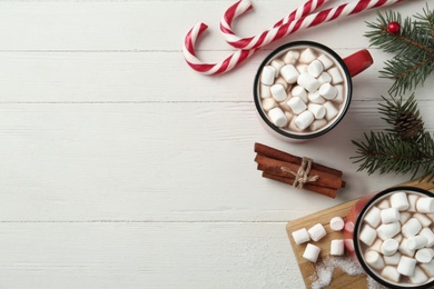 Hot drinks with marshmallows, candy canes and fir branches on white wooden table, flat lay. Space for text
