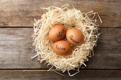 Eggs with words PENSION, RETIRE and 401k in nest on wooden background, top view