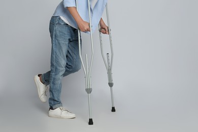 Man with injured leg using crutches on grey background, closeup. Space for text