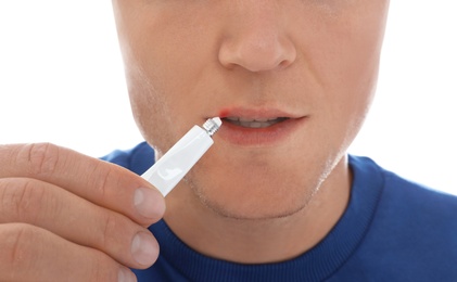 Man with cold sore applying cream on lips against white background, closeup