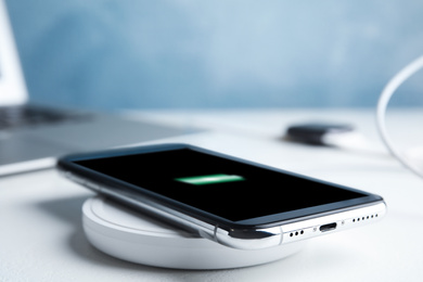 Mobile phone charging with wireless pad on white stone table, closeup. Space for text