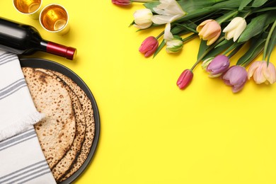 Tasty matzos, wine and fresh flowers on yellow background, space for text. Passover (Pesach) celebration