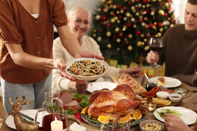 Woman with bowl of traditional Christmas kutia and her family at festive dinner, focus on hands. Slavic dish