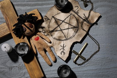 Female voodoo doll with heart and ceremonial items on grey wooden table, flat lay