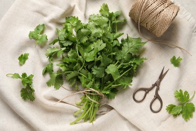 Fresh green cilantro, twine and scissors on white fabric, flat lay