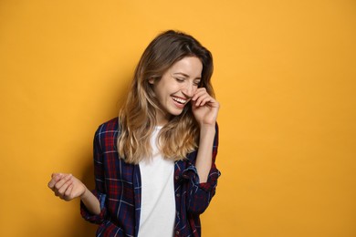 Cheerful young woman laughing on yellow background