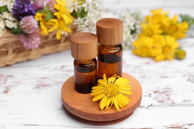 Bottles of essential oils and beautiful flowers on white wooden table