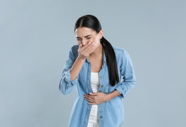Woman suffering from stomach ache and nausea on grey background. Food poisoning