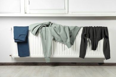 Pants, hoodie and turtleneck sweater on heating radiator near window indoors