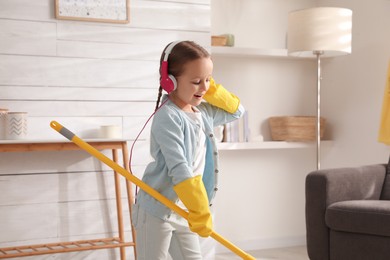 Cute little girl in headphones with mop singing while cleaning at home